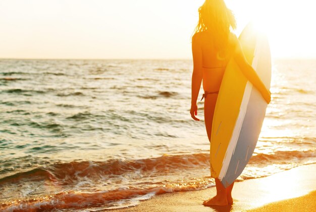 Jonge sportieve vrouw met surfplank aan zeekust