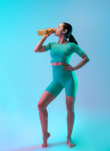 Jonge sportieve vrouw opleiding en drinkwater, geïsoleerd op de achtergrond van de gradiëntstudio in neonlicht