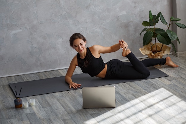 Jonge sportieve vrouwelijke yoga-instructeur online coaching, video maken van yogalessen op laptopcamera