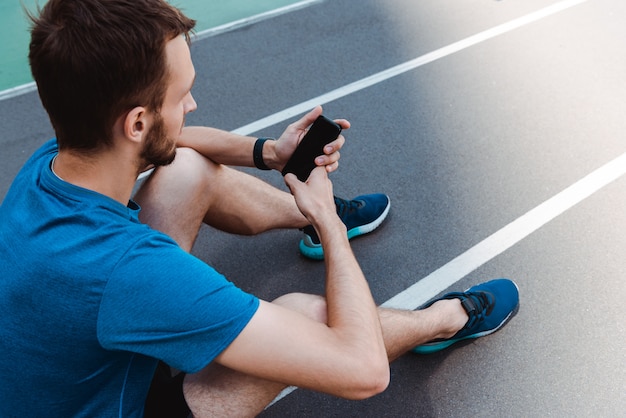 jonge sportman zittend op de atletiekbaan en het gebruik van smartphone