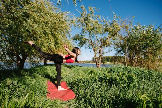 Foto jonge sportvrouw die buiten yoga beoefent aan de oever van het meer