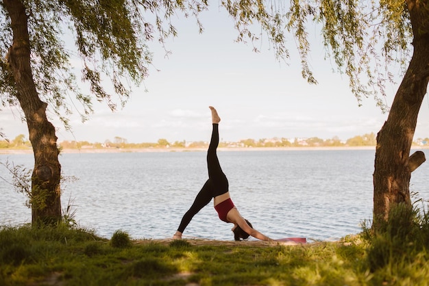 Jonge sportvrouw die buiten yoga beoefent aan de oever van het meer