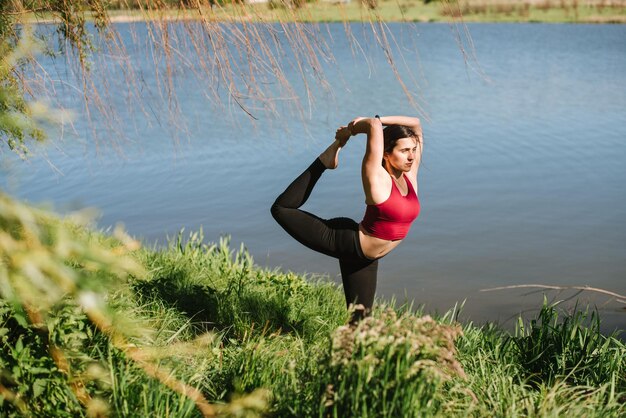 Jonge sportvrouw die buiten yoga beoefent aan de oever van het meer