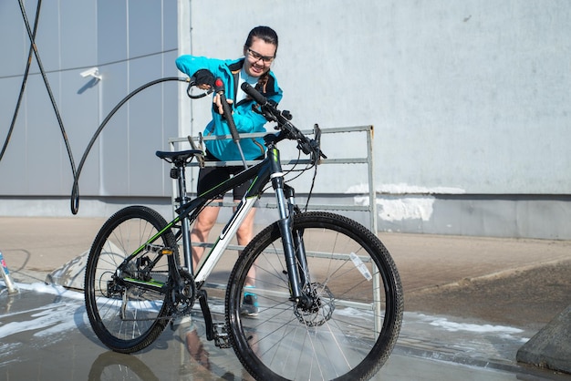 Jonge sportvrouw die fiets wast bij selfservice car wash