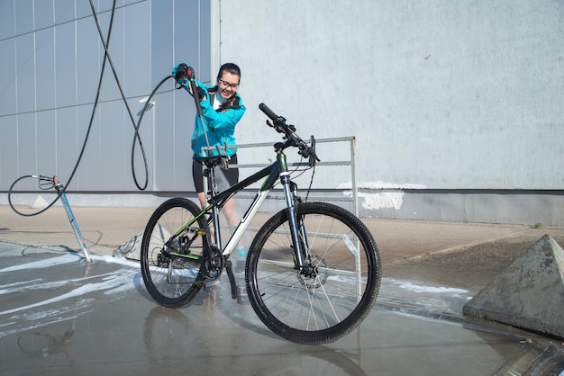 Jonge sportvrouw die fiets wast bij selfservice car wash