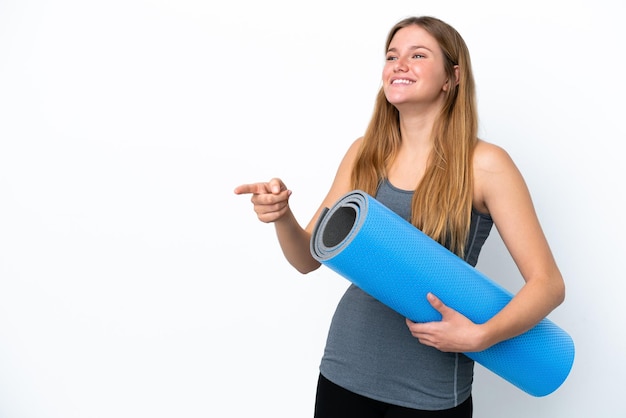 Jonge sportvrouw die naar yogalessen gaat terwijl ze een mat naar de zijkant wijst en een product presenteert