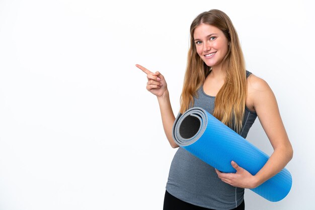 Jonge sportvrouw die naar yogalessen gaat terwijl ze een mat naar de zijkant wijst