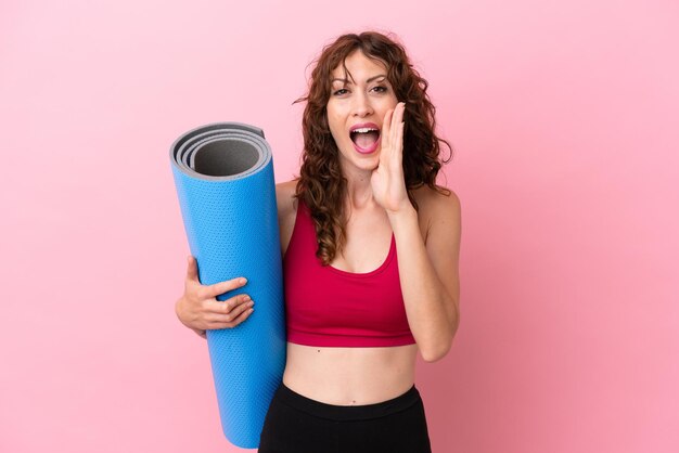 Jonge sportvrouw die naar yogalessen gaat terwijl ze een mat vasthoudt die op een roze achtergrond wordt geïsoleerd en met wijd open mond schreeuwt