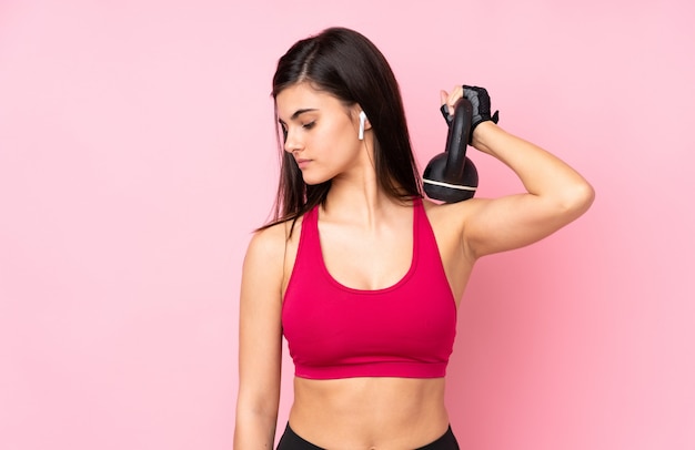 Jonge sportvrouw die over roze muur gewichtheffen met kettlebell maakt