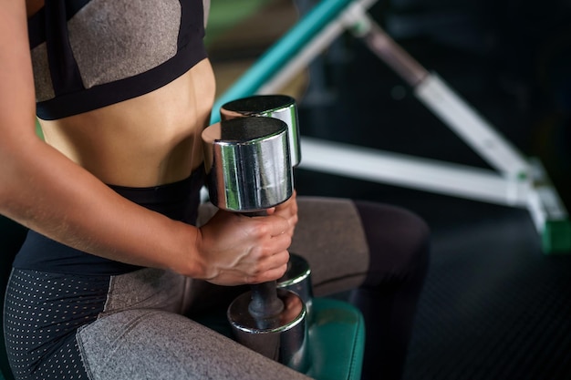 Jonge sportvrouw doet oefeningen met halters zittend op een bankje in de sportschool. Fitness