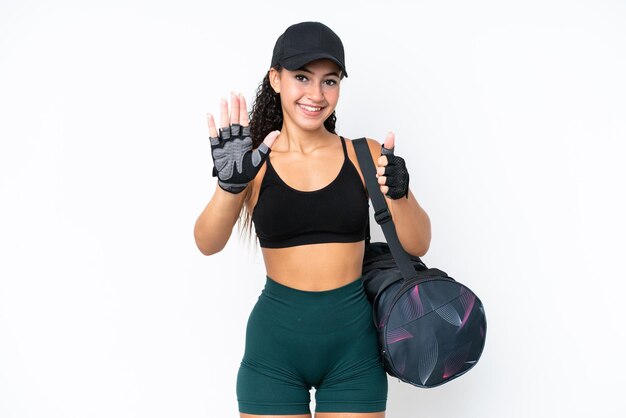 Jonge sportvrouw met sporttas die op witte achtergrond wordt geïsoleerd die zes met vingers telt