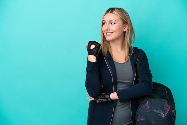 Jonge sportvrouw met sporttas geïsoleerd op een blauwe achtergrond die naar de zijkant wijst om een product te presenteren