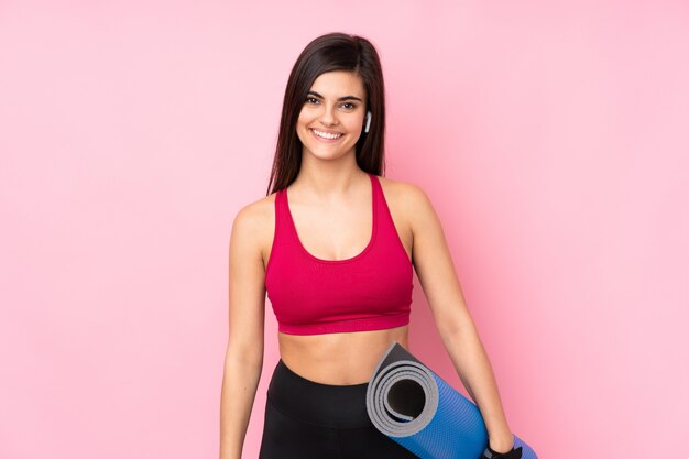 Jonge sportvrouw over geïsoleerde roze muur met een mat en het glimlachen