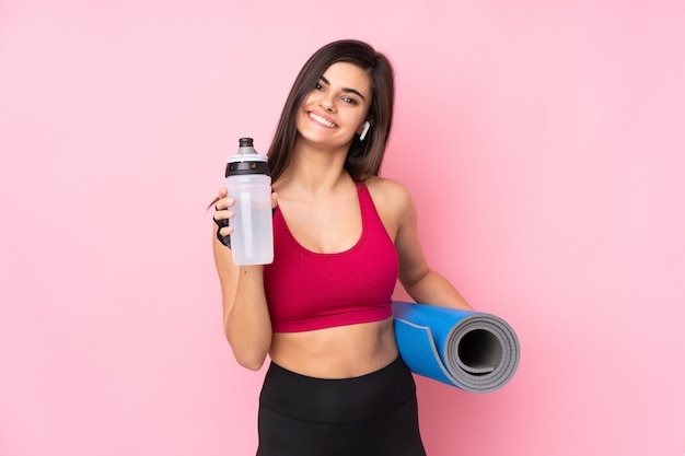 Jonge sportvrouw over roze muur met de fles van het sportenwater en met een mat