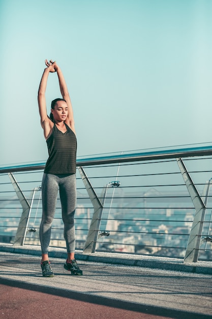 Jonge sportvrouw warming-up op de brug en handen omhoog