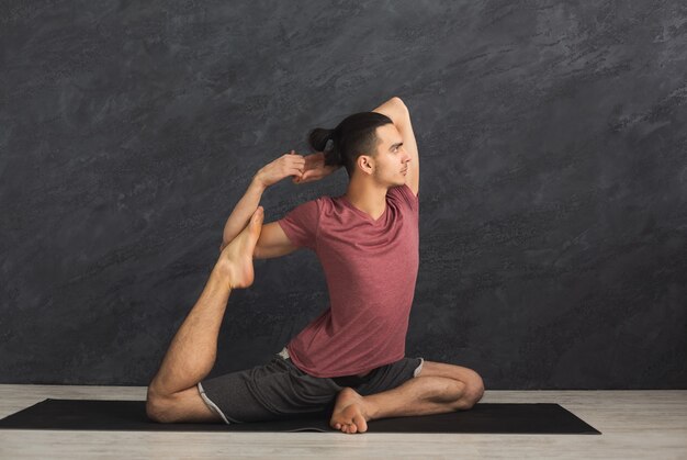 Jonge sterke man die yoga beoefent, in flexibele pose staat op mat in fitnessles, asana-oefening maakt, ruimte kopieert