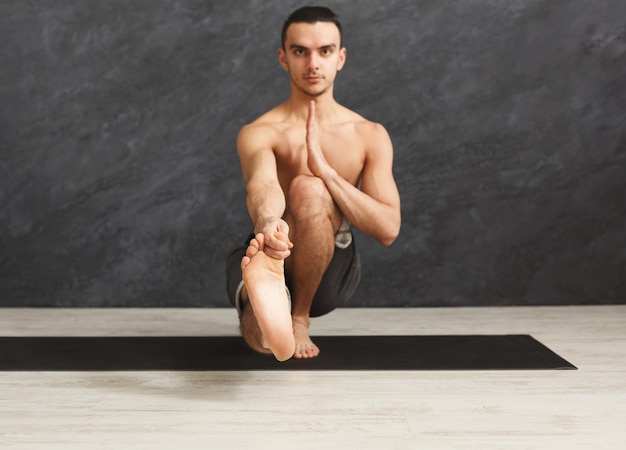 Jonge sterke man die yoga beoefent, in flexibele pose staat op mat in fitnessles, balans maakt en rekoefeningen doet, kopieer ruimte