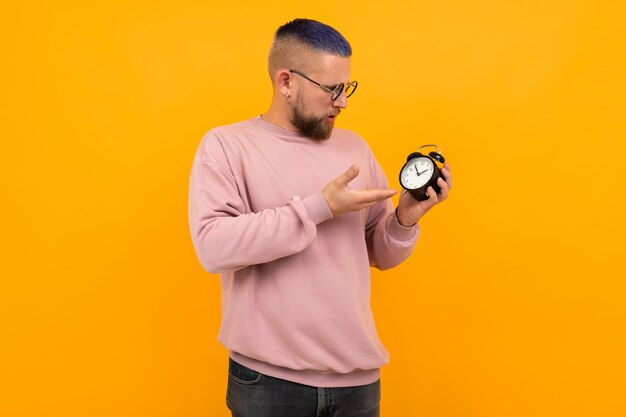 Jonge sterke man met kort zwart haar en bril houdt wekker en glimlacht