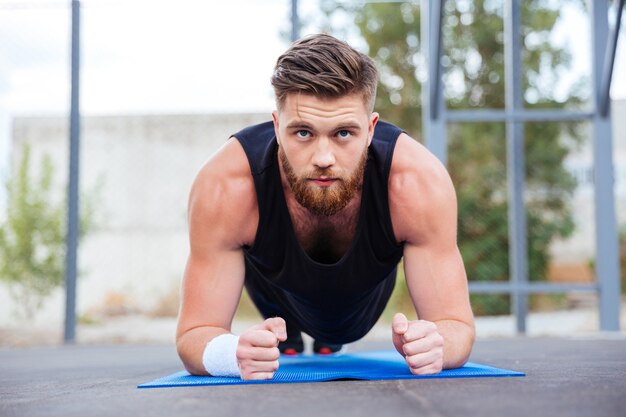 Jonge sterke sportman doet plankoefening op blauwe fitnessmat tijdens training buitenshuis