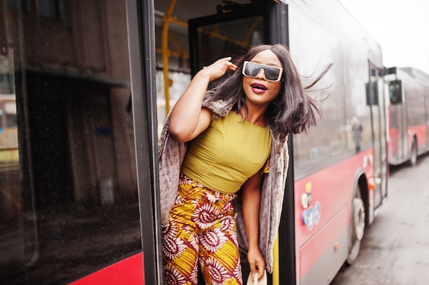 Jonge stijlvolle afro-amerikaanse vrouw in moderne zonnebril rijden op een bus.