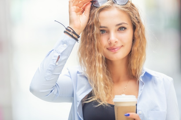 Jonge stijlvolle blonde koffie drinken om te gaan glimlachen en wandelen langs de straat.