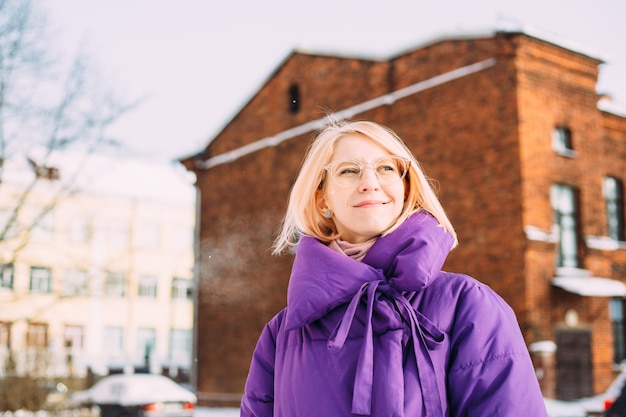 Jonge stijlvolle blonde met bril op straat in de sneeuw