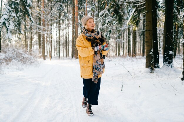 Jonge stijlvolle hipster meisje in gele jas met een warme sjaal wandelen in het sneeuwwoud