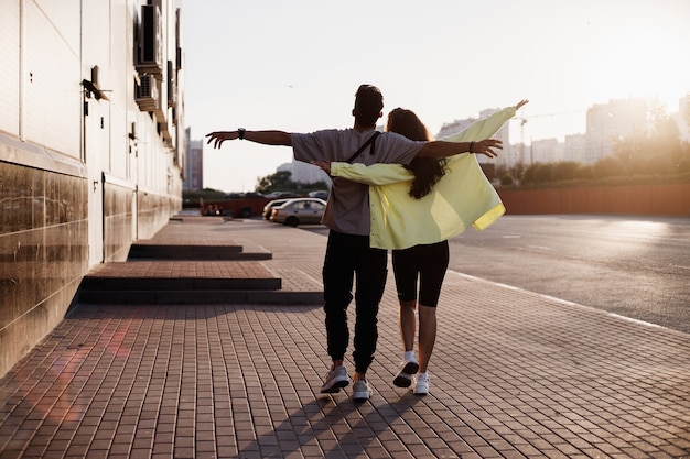 Jonge stijlvolle jongen en meisje lopen samen op het plein om te parkeren naast het gebouw op de zonsondergang.