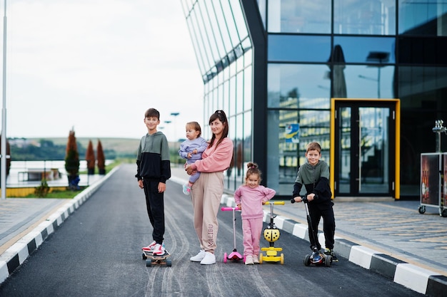 Jonge stijlvolle moeder met vier kinderen buiten Sportfamilie brengt vrije tijd buiten door met scooters en skates