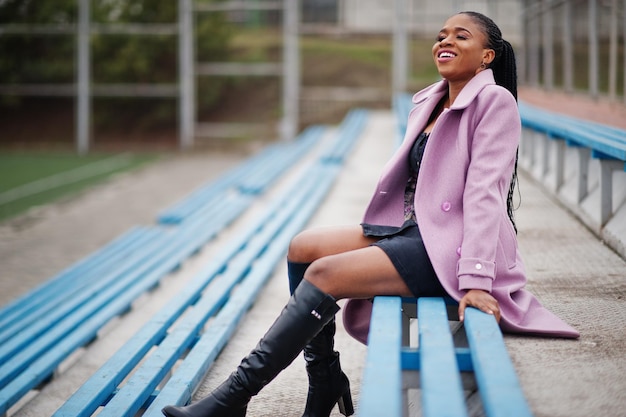 Jonge, stijlvolle, mooie afro-amerikaanse vrouw in de straat bij de tribunes van het stadion met een mode-outfitjas