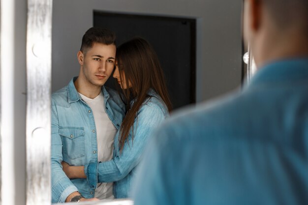 Jonge stijlvolle paar in denim in de buurt van vintage spiegel met verlichting