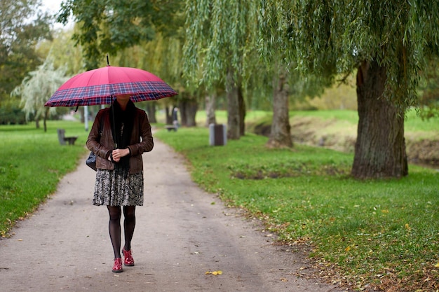 Foto jonge stijlvolle vrouw die in het herfstpark loopt met een enorme rode paraplu