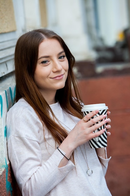 Jonge stijlvolle vrouw drinkt thee in een stadsstraat Hipster Europees meisje met latte papieren glas in s