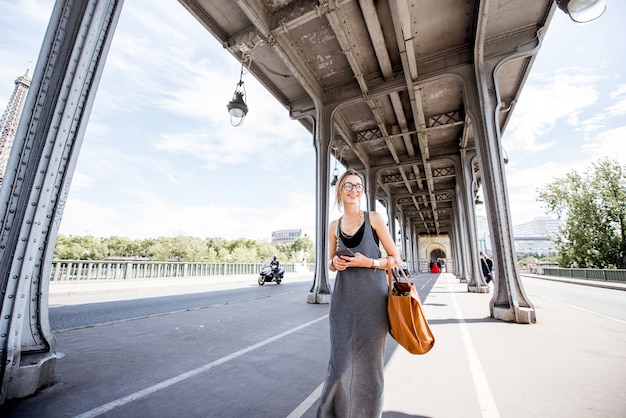 Jonge stijlvolle vrouw met telefoon en tas op de beroemde oude brug met prachtig uitzicht op de Eiffeltoren in Parijs