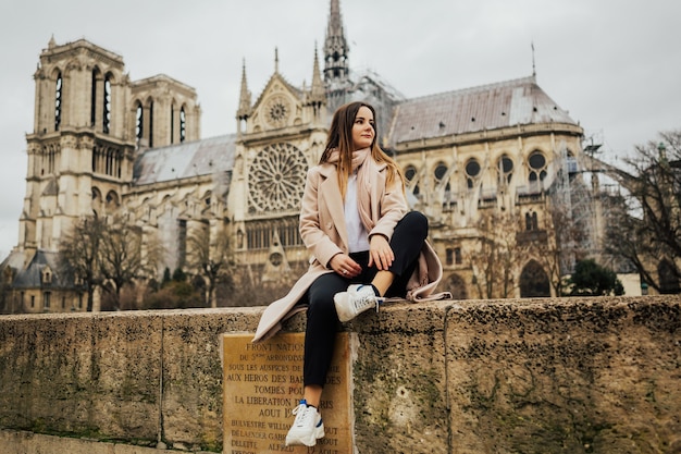 Jonge stijlvolle vrouw toeristische zitten in de buurt van de beroemde kathedraal notre dame in parijs, frankrijk.