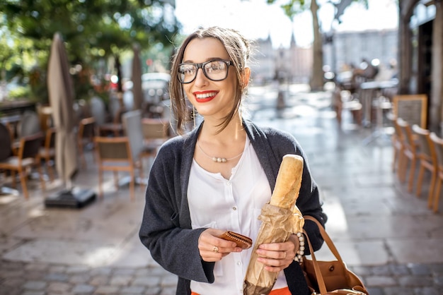 Jonge stijlvolle vrouw wandelen met stokbrood op de mooie straat in franse stad