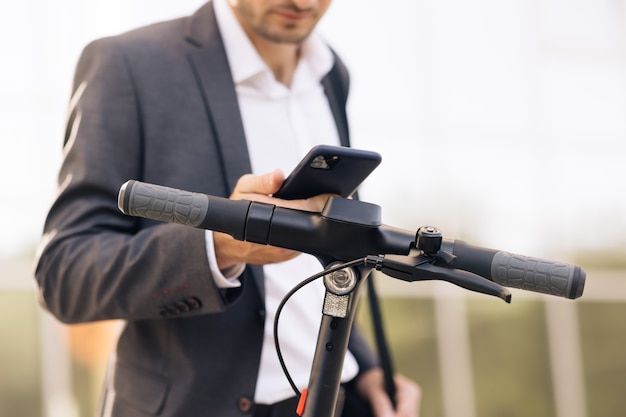 Jonge stijlvolle zakenman met telefoon en een elektrische scooter zakenman huurt elektrische scooter met...