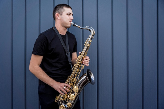 Jonge straatmuzikant die saxofoon speelt bij de grote blauwe muur