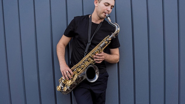 Jonge straatmuzikant die saxofoon speelt bij de grote blauwe muur