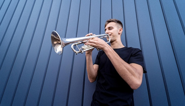 Jonge straatmuzikant die trompet speelt bij de grote blauwe muur