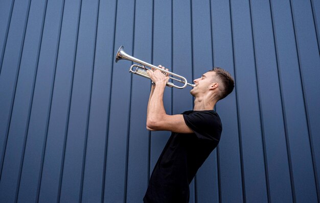 Jonge straatmuzikant die trompet speelt bij de grote blauwe muur