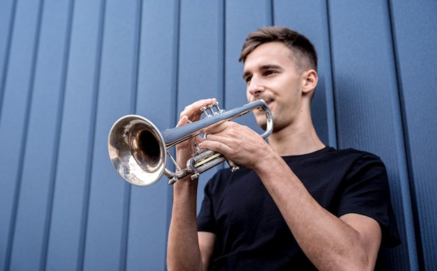 Jonge straatmuzikant die trompet speelt bij de grote blauwe muur