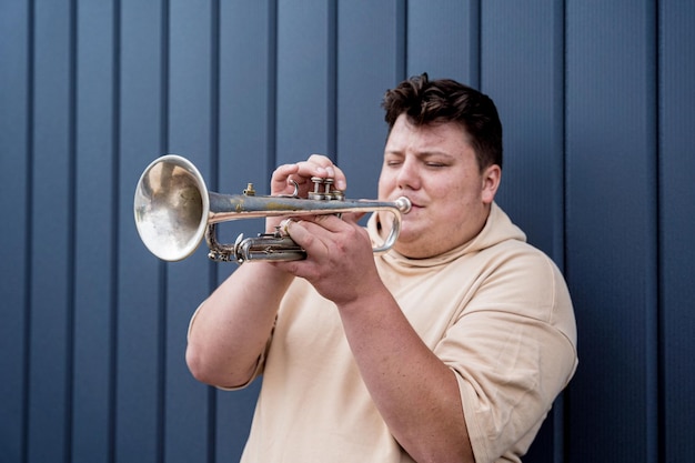 Jonge straatmuzikant die trompet speelt bij de grote blauwe muur