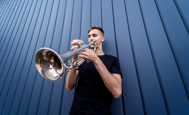 Jonge straatmuzikant die trompet speelt bij de grote blauwe muur