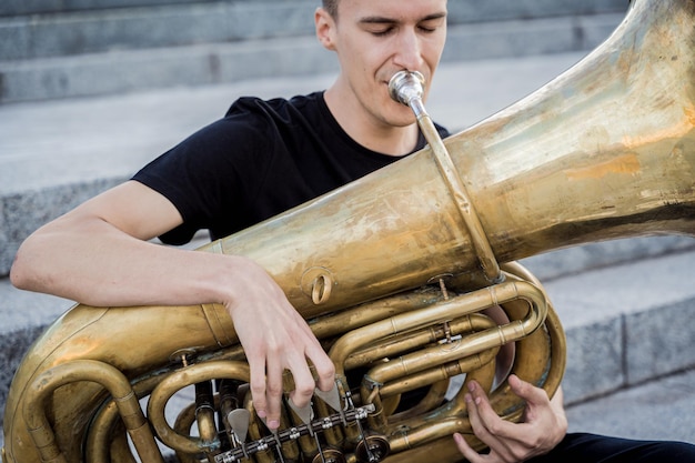 Jonge straatmuzikant speelt tuba zittend op granieten treden