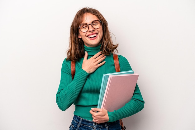 Jonge student blanke vrouw geïsoleerd op een witte achtergrond lacht hardop terwijl ze de hand op de borst houdt