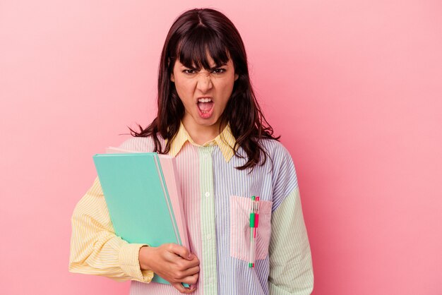 Jonge student blanke vrouw met boeken geïsoleerd op roze achtergrond schreeuwen erg boos en agressief.