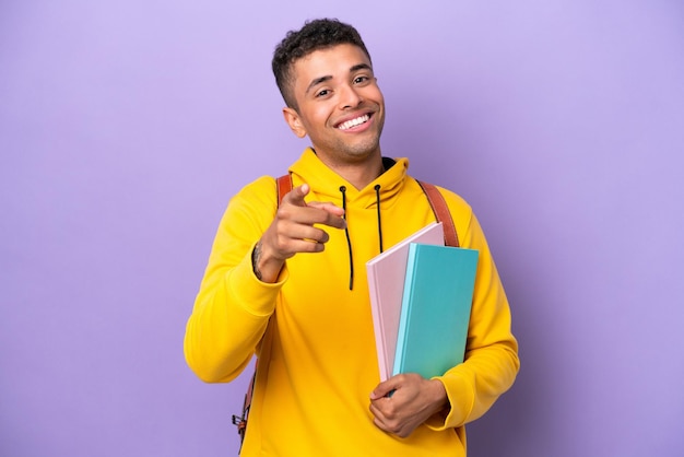 Jonge student Braziliaanse man geïsoleerd op paarse achtergrond wijzend naar voren met gelukkige uitdrukking