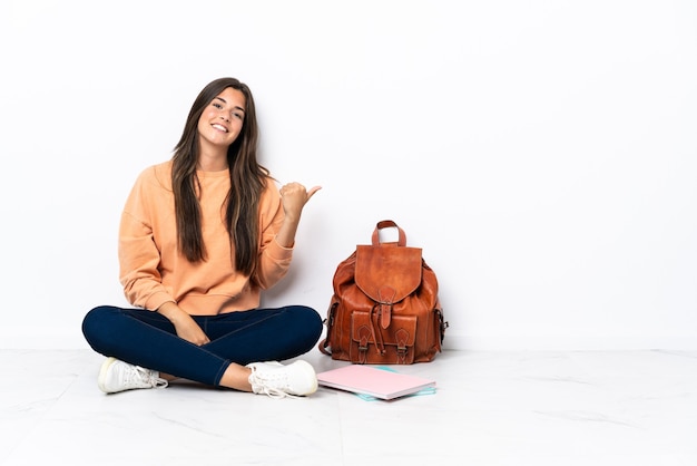 Jonge student Braziliaanse vrouw zittend op de vloer wijst naar de zijkant om een product te presenteren