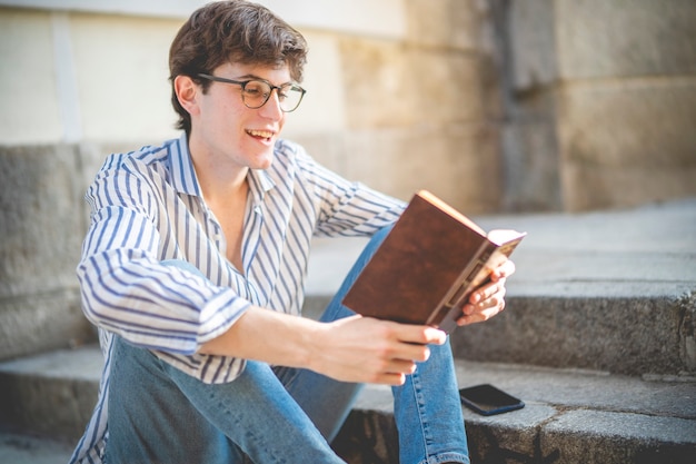 Foto jonge student die een boek leest op de trappen van een gebouw